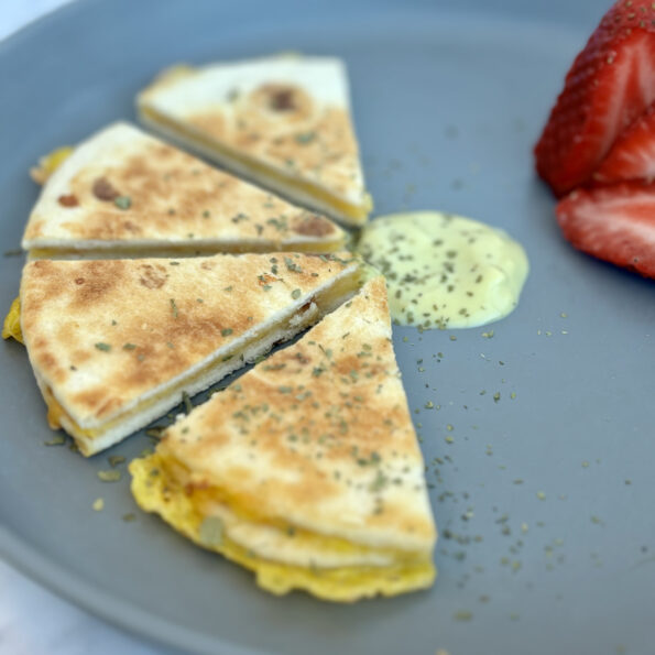 Wedges of an egg, cheese, and avocado quesadilla, sided with an avocado yogurt sauce and strawberries.