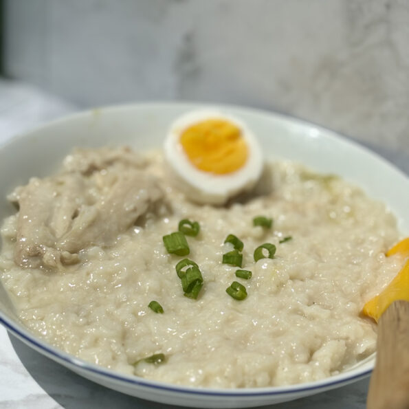 A bowl of glutinous rice porridge, with chicken pieces at left and a hard-boiled egg at the top of the bowl