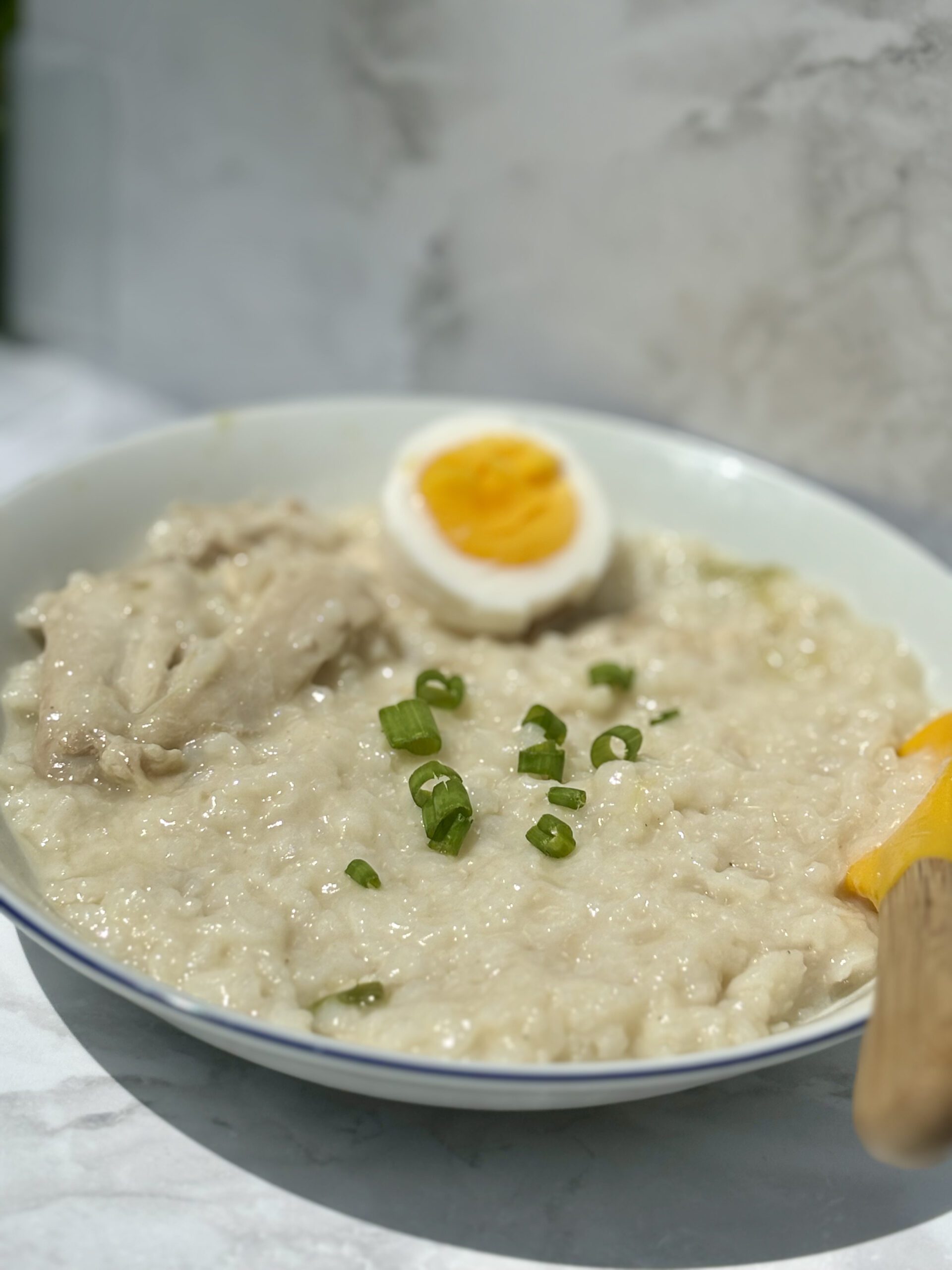 A bowl of glutinous rice porridge, with chicken pieces at left and a hard-boiled egg at the top of the bowl