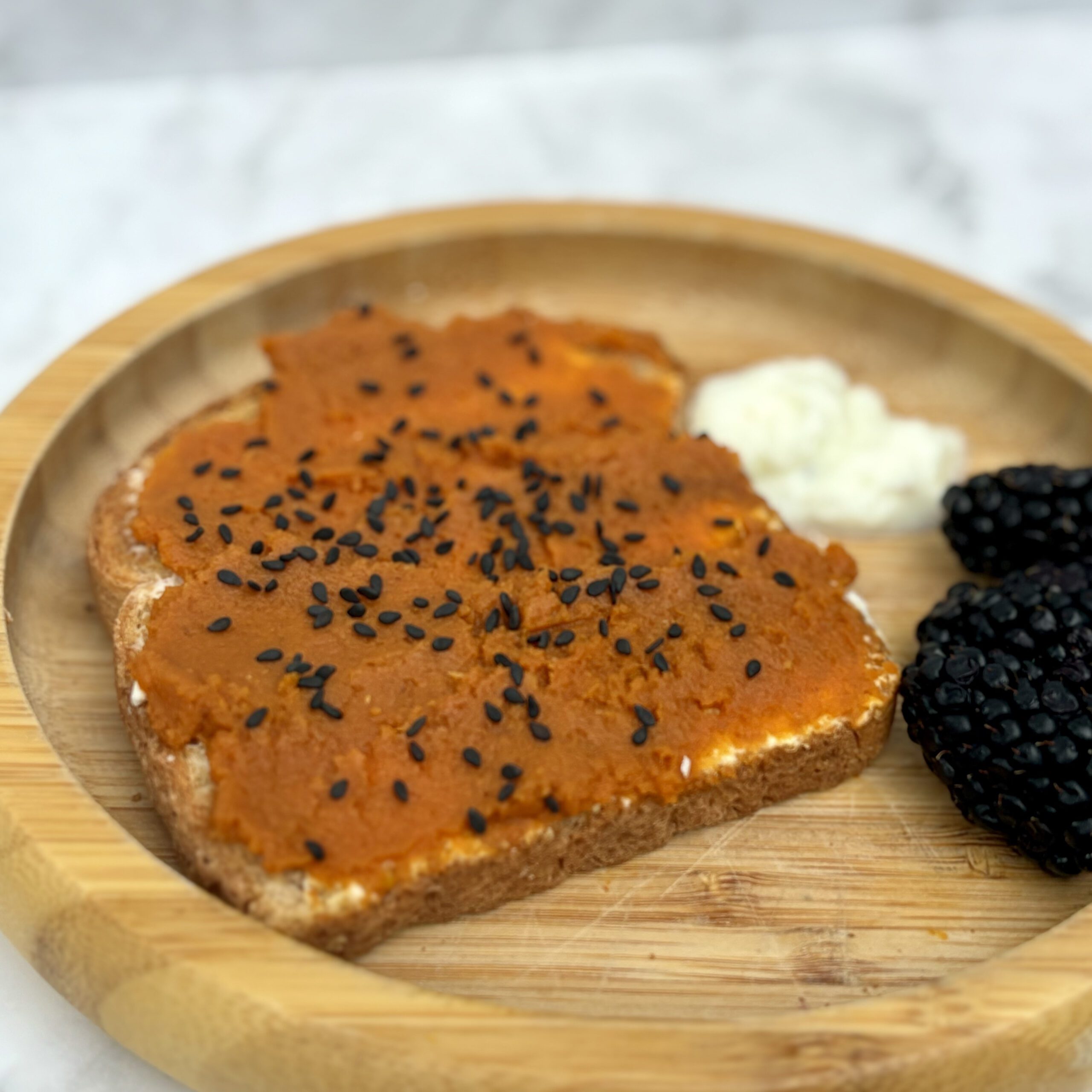 A slice of toast covered in layers of whipped cottage cheese and pumpkin butter is displayed on a plate.