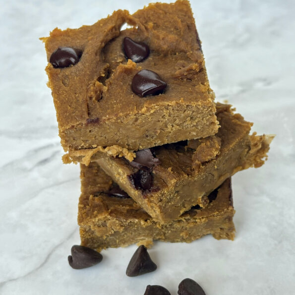 Three chickpea blondies stacked on top of one another, with chocolate chips scattered around them.