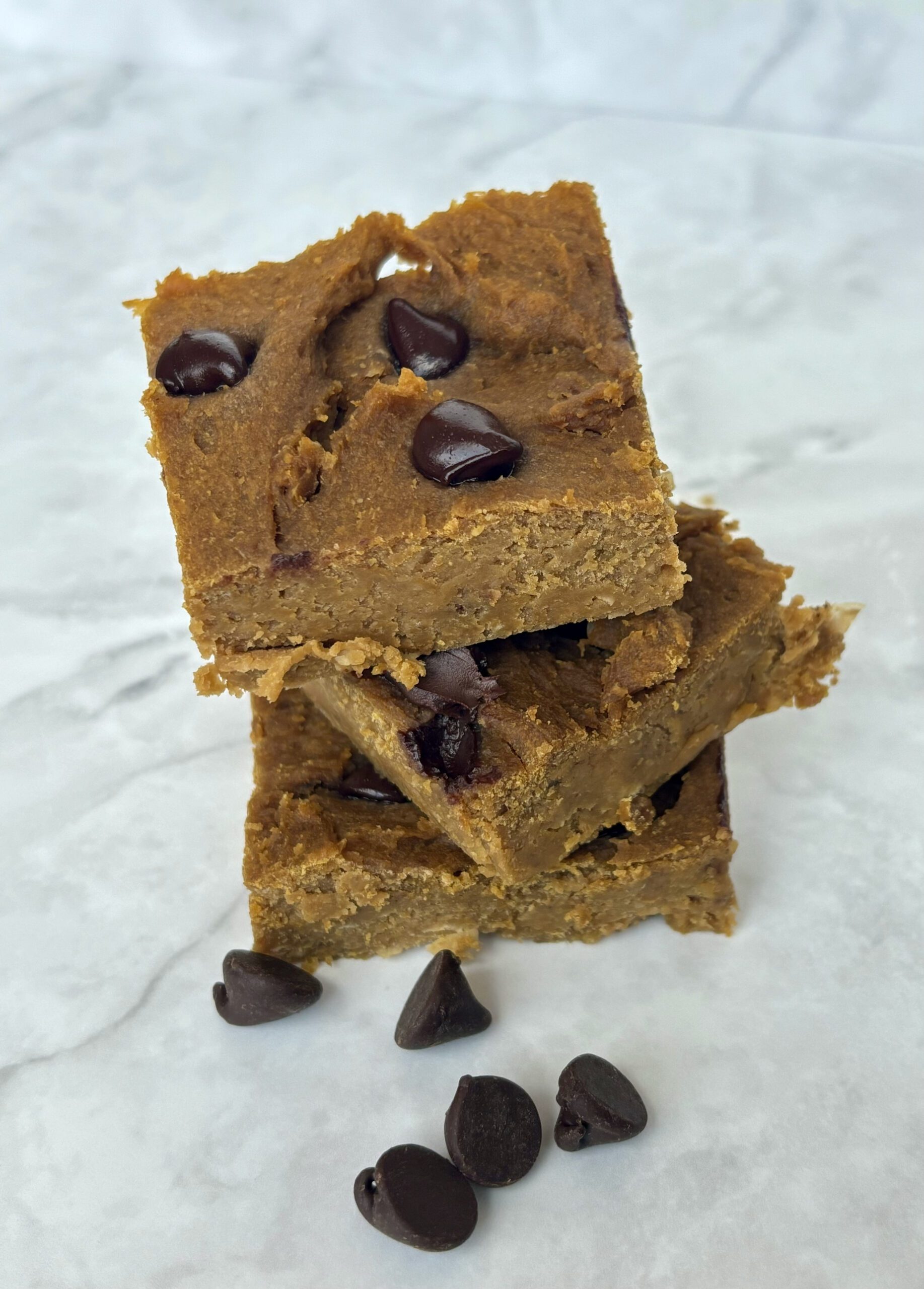 Three chickpea blondies stacked on top of one another, with chocolate chips scattered around them.