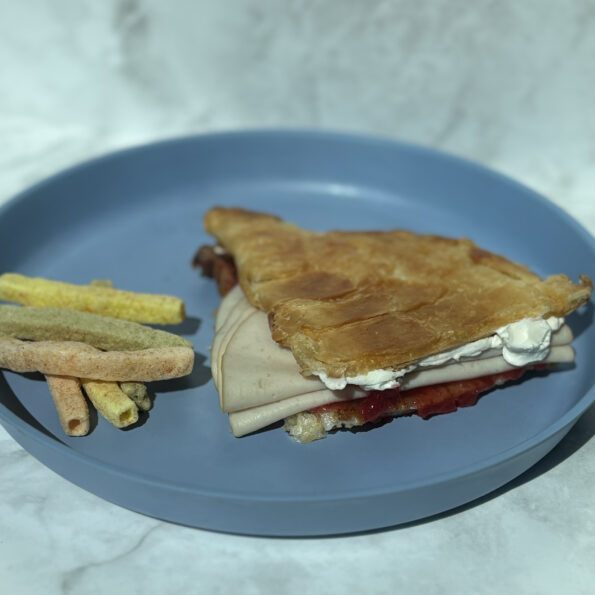 A picture of a turkey, cream cheese, and jelly sandwich on croissant, with veggie sticks on the side.