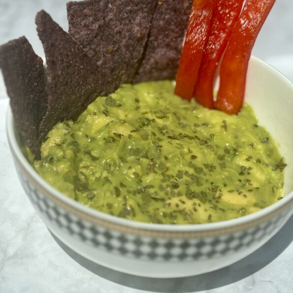 A bowl of guacamole, with chips and red pepper slices stuck in it