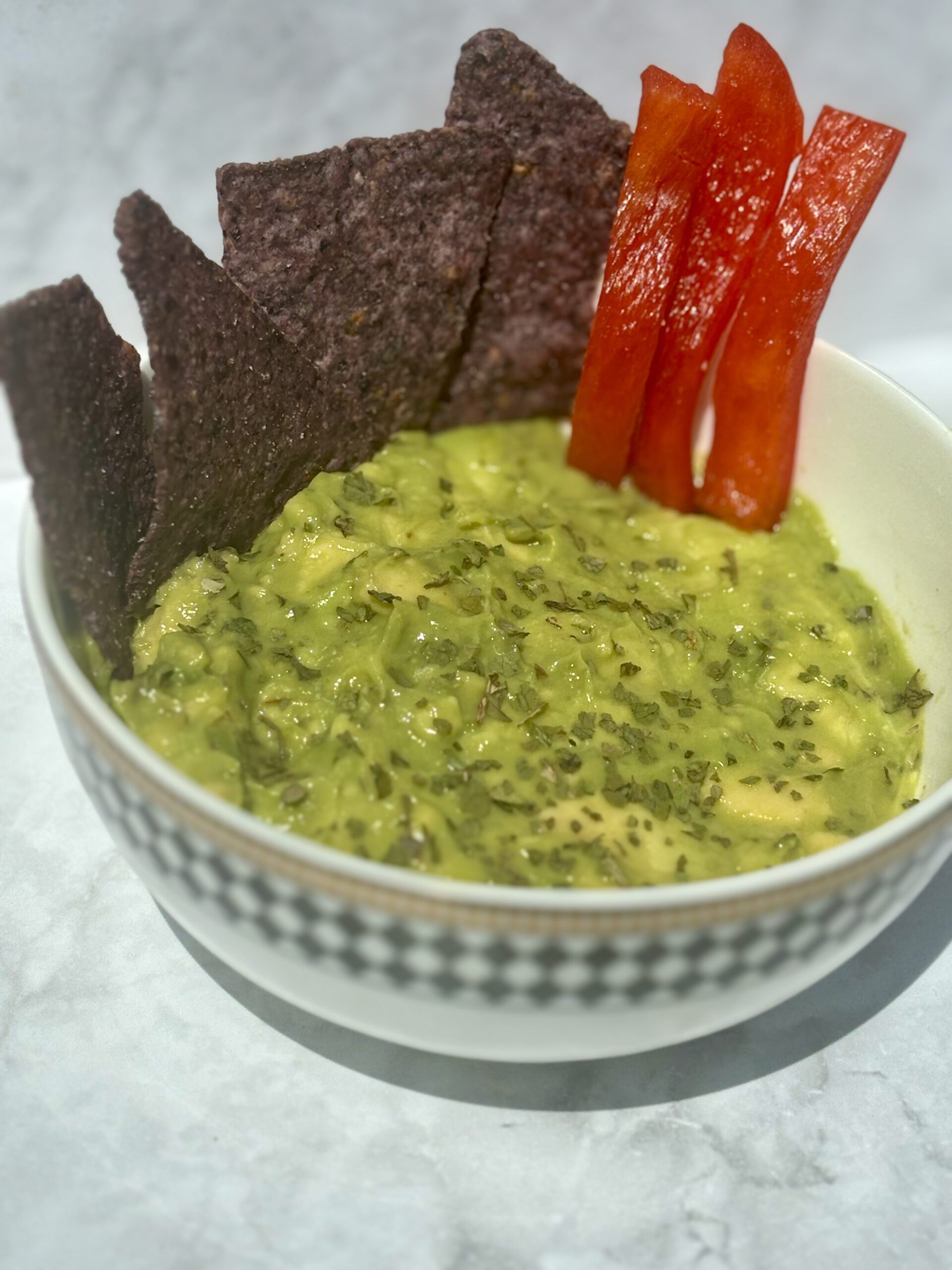 A bowl of guacamole, with chips and red pepper slices stuck in it