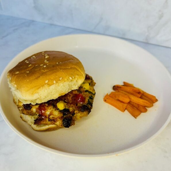 A chicken teriyaki burger, dotted with ketchup and mustard, is paired on a plate with carrot fries.