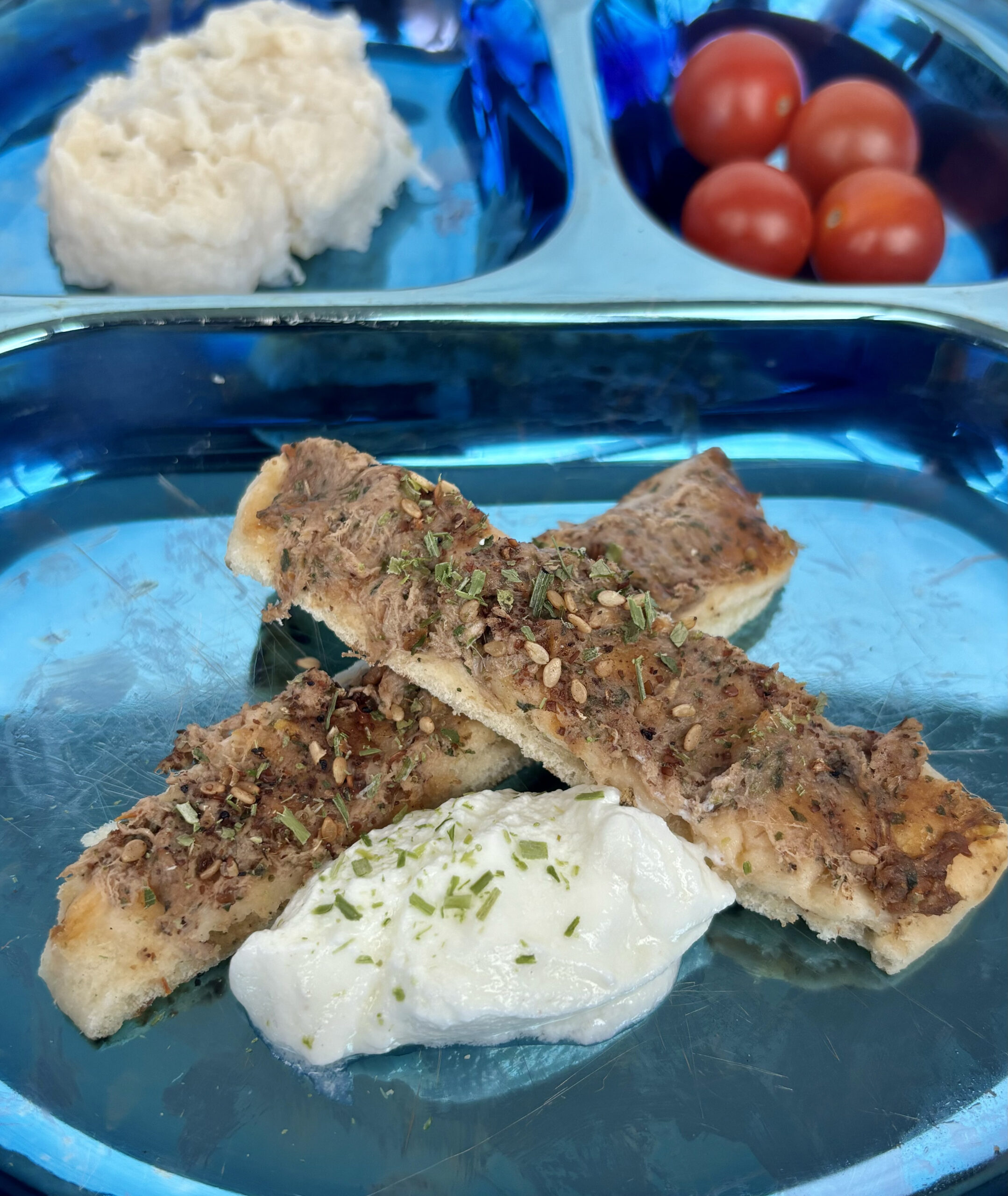 Meat and veggie flatbread, cut into strips and sided with garlic yogurt sauce, is presented on a plate.