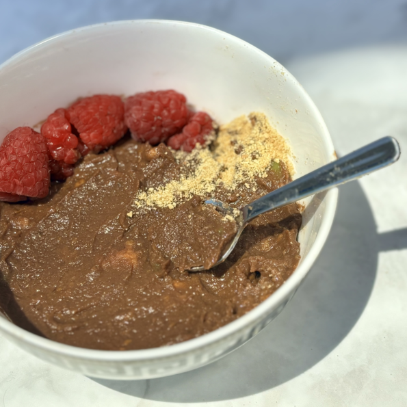 A close-up of the avocado and sweet potato chocolate pudding, featuring raspberries and a dusting of graham cracker crumbs.