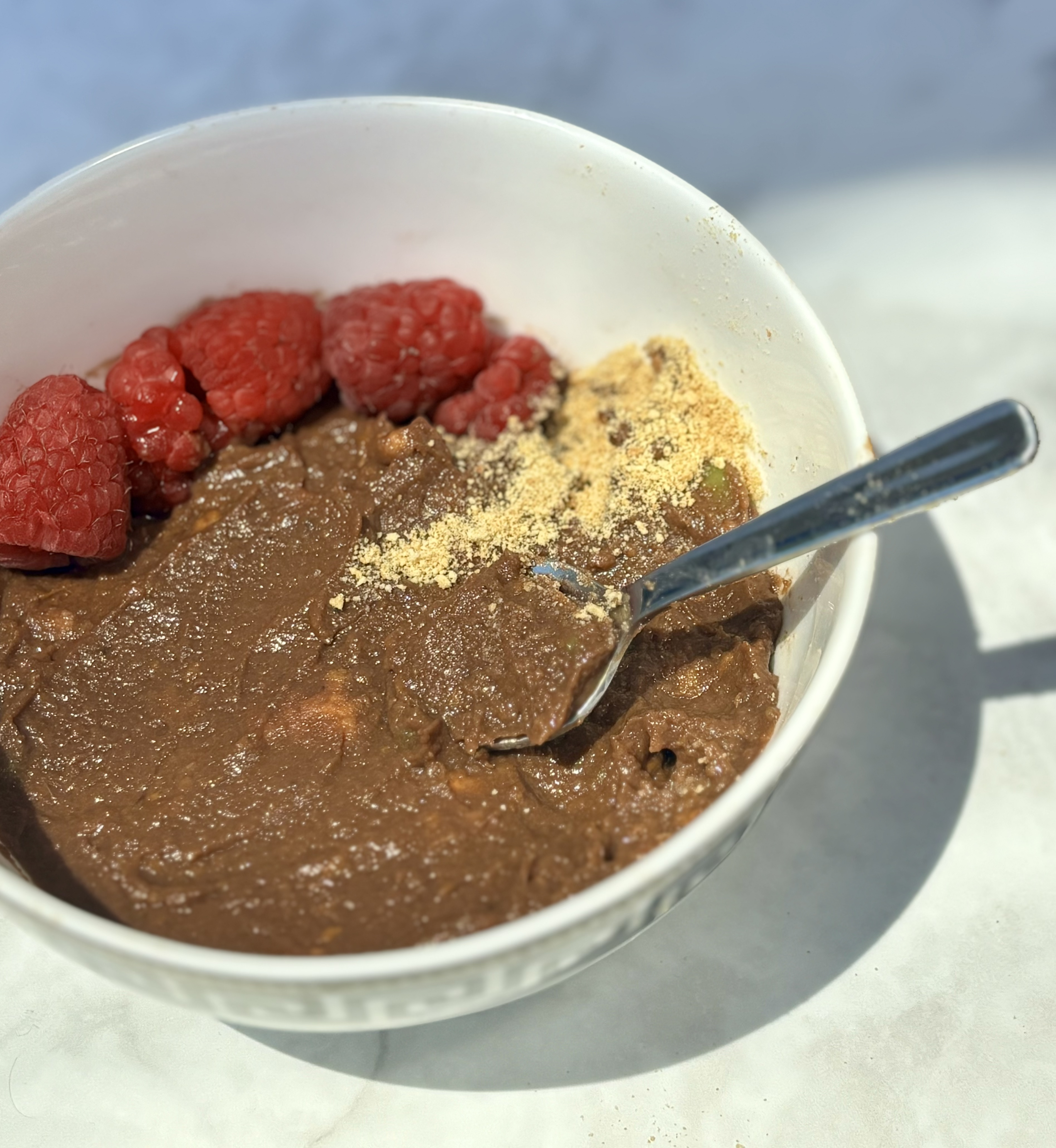 A close-up of the avocado and sweet potato chocolate pudding, featuring raspberries and a dusting of graham cracker crumbs.