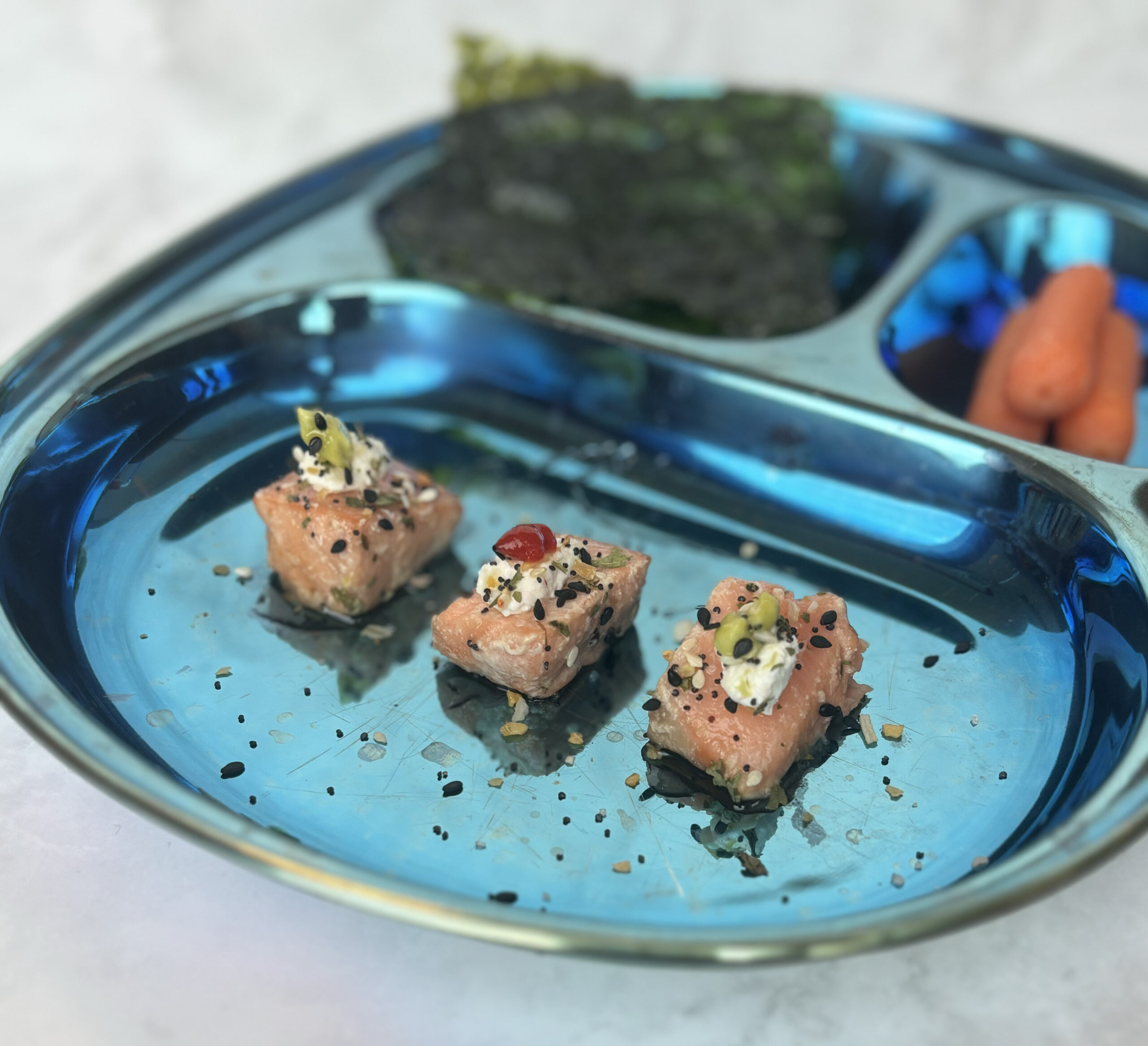 A plate with three everything salmon bites, plus seaweed and baby carrots.