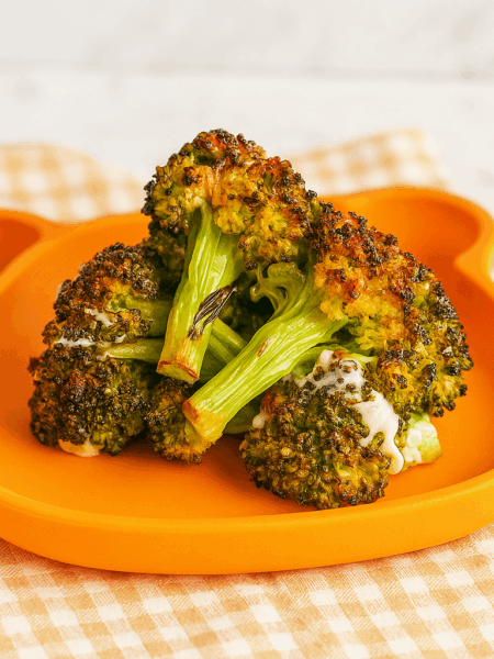 A stack of broiled broccoli for kids shown on a toddler plate.