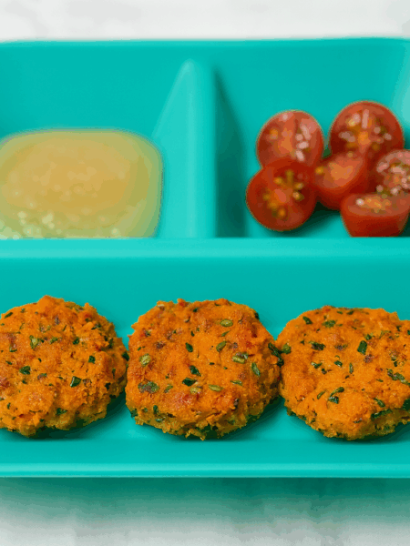 A plate shows a trio of salmon and sweet potato cakes, along with applesauce and grapes.