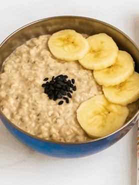 A bowl of toddler overnight oats, studded with banana slices and black sesame seeds.