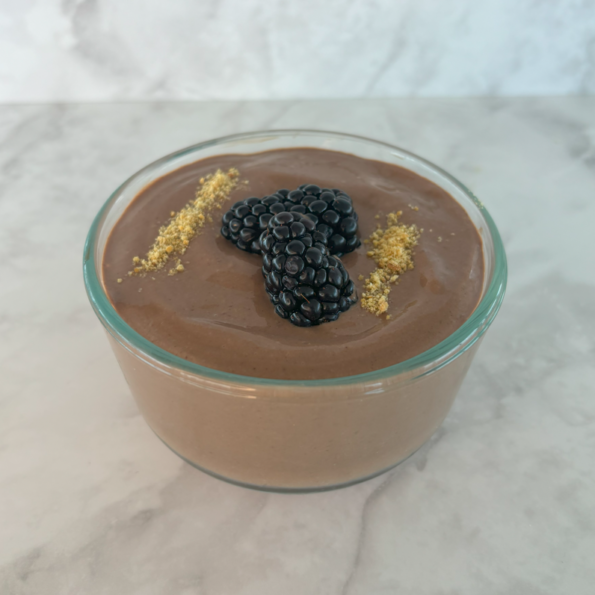 A clear ramekin filled with chocolate peanut butter mousse made with tofu, then topped with blackberries and graham cracker crumbs