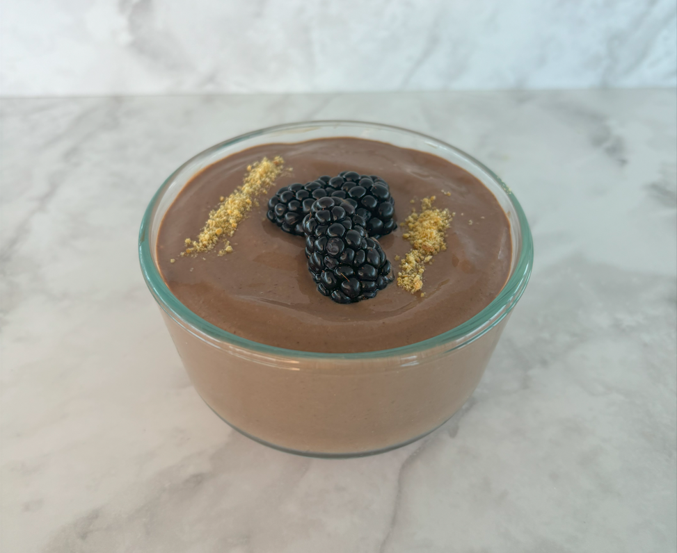 A clear ramekin filled with chocolate peanut butter mousse made with tofu, then topped with blackberries and graham cracker crumbs