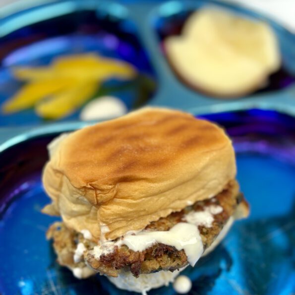 A crabcake sandwich sits in the foreground, with tartar sauce dripping off it.