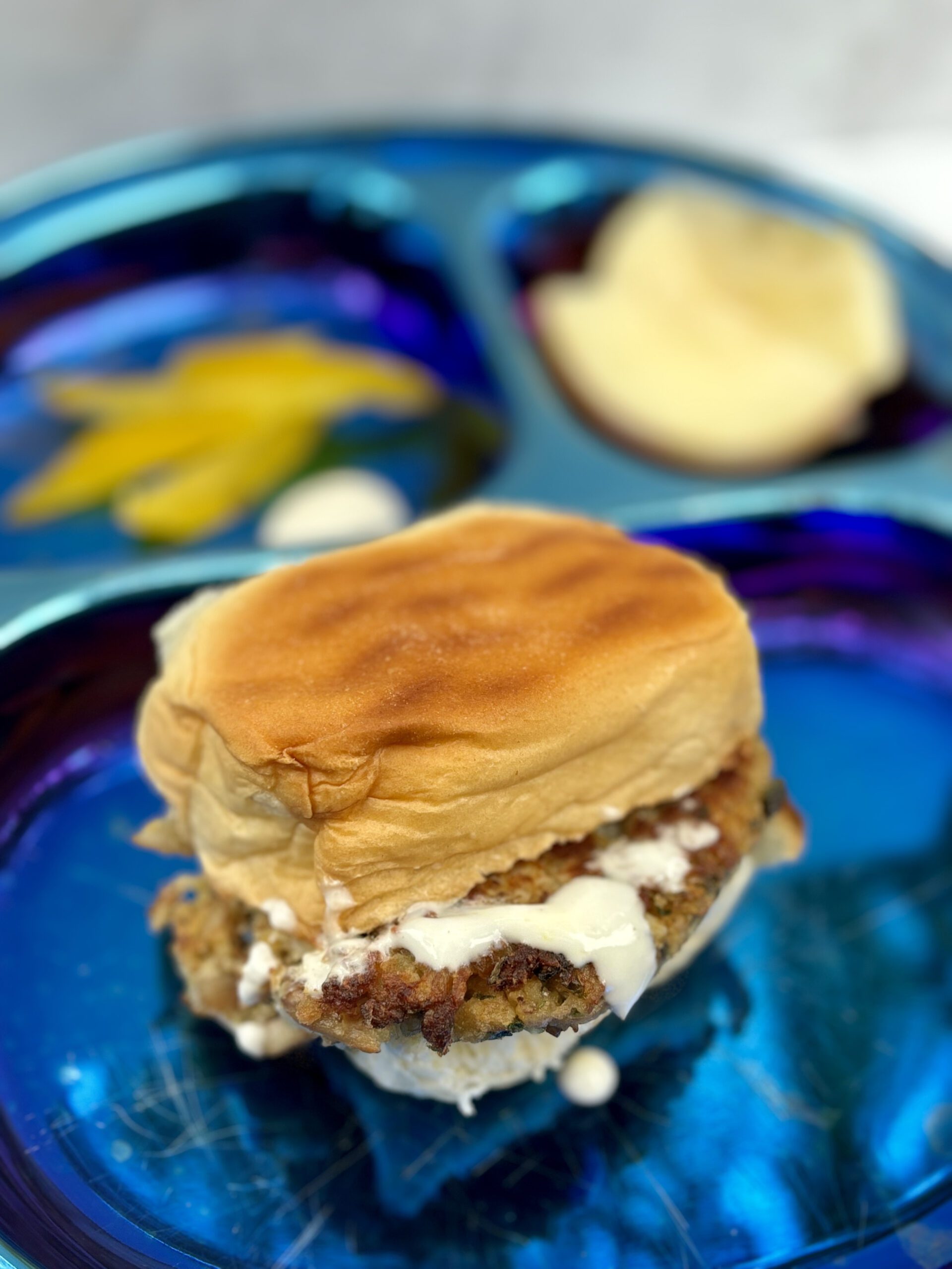 A crabcake sandwich sits in the foreground, with tartar sauce dripping off it.