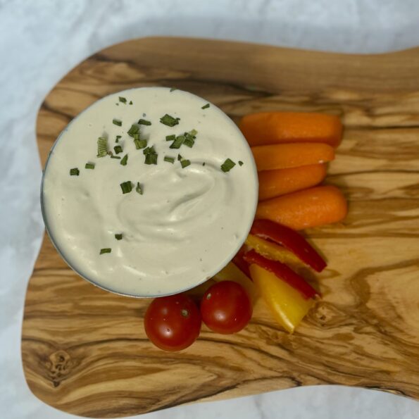 A bowl of tofu-cashew whip is topped with herbs and sided with baby carrots, strips of bell pepper, and cherry tomatoes