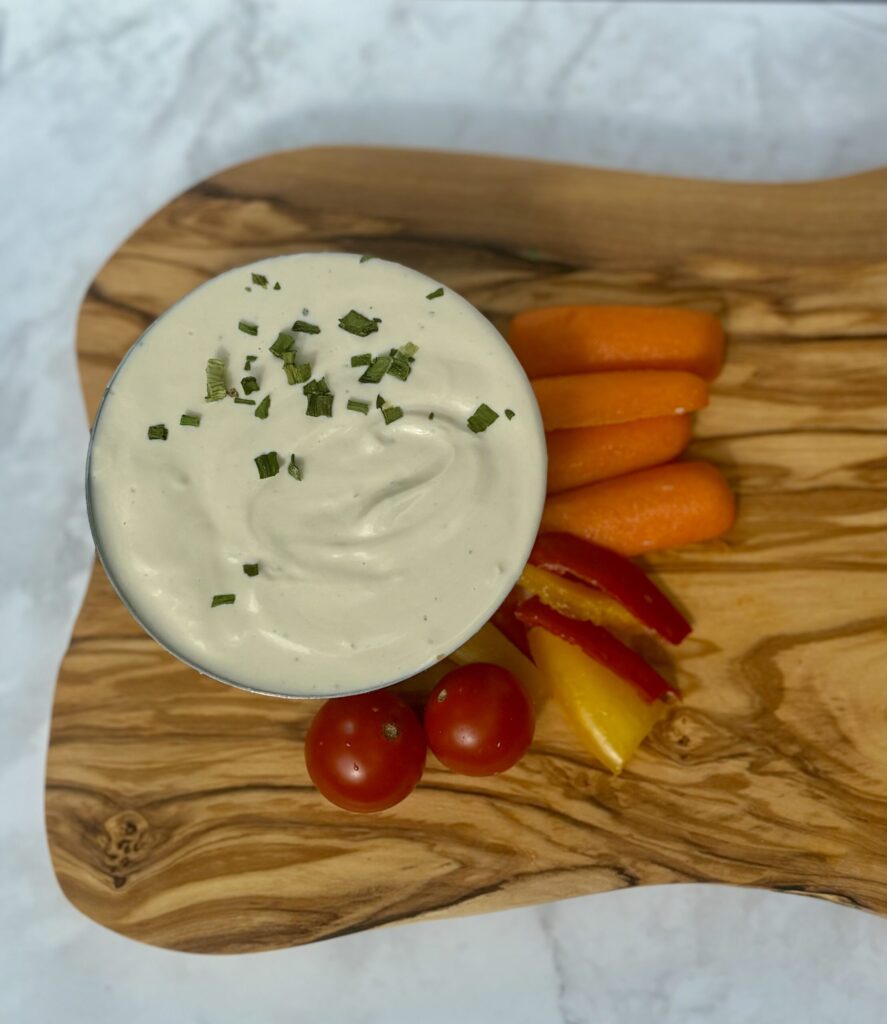 A bowl of tofu-cashew whip is topped with herbs and sided with baby carrots, strips of bell pepper, and cherry tomatoes