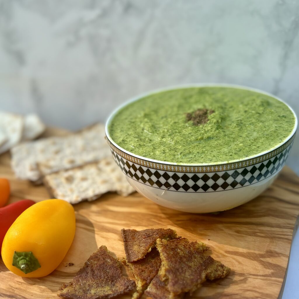 A bowl of spinach and cheese curry is sided with various raw vegetables and breads