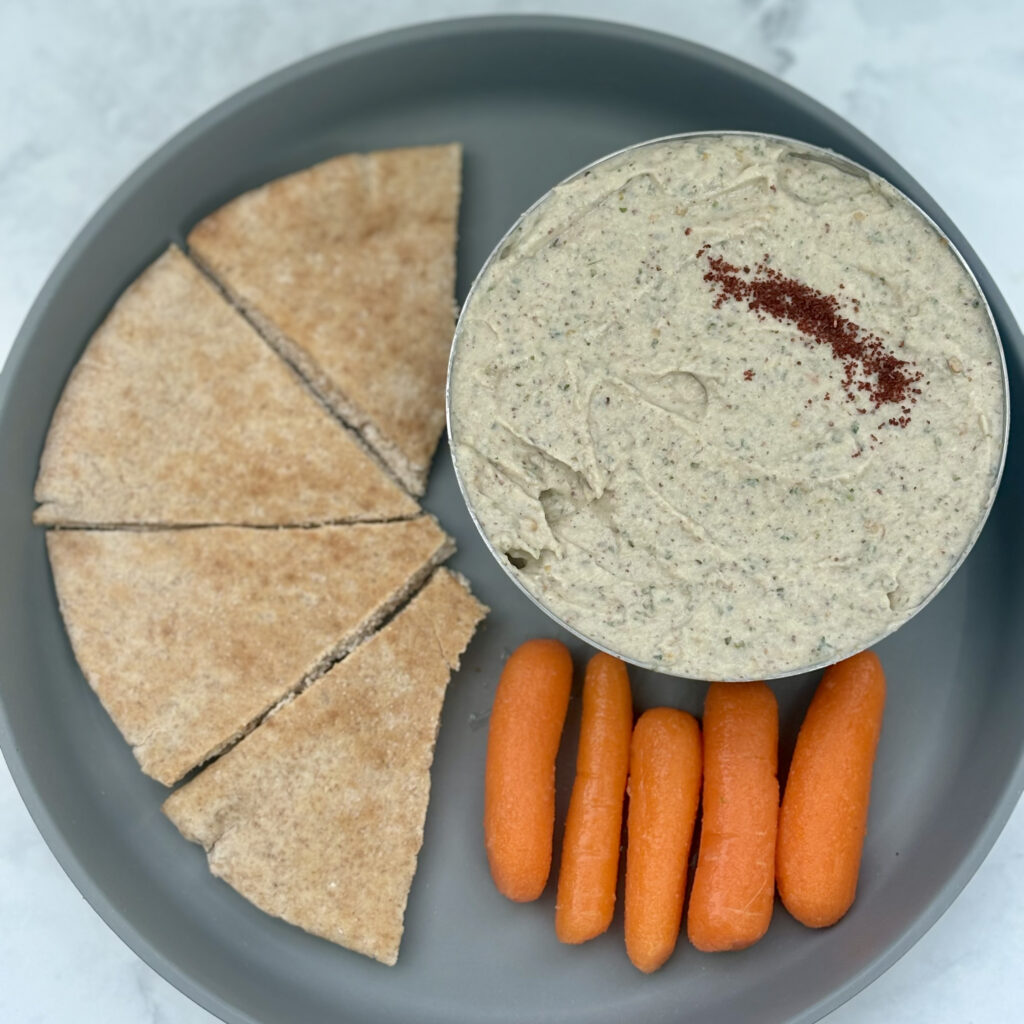 A bowl of baba ghanoush is presented with pita triangles and baby carrot sticks.