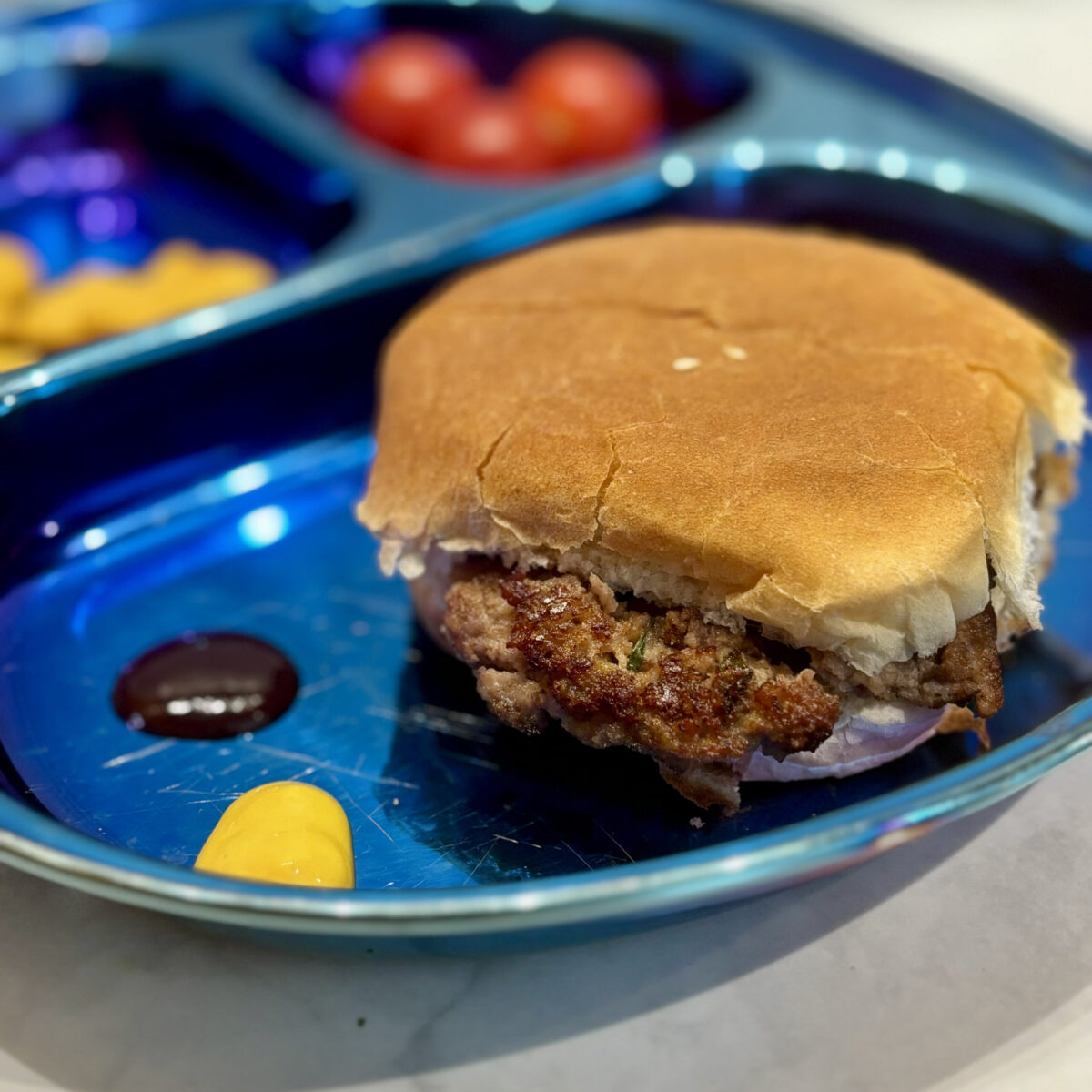 A smashed turkey burger sits on a bun, sided by dollops of mustard and barbecue sauce.