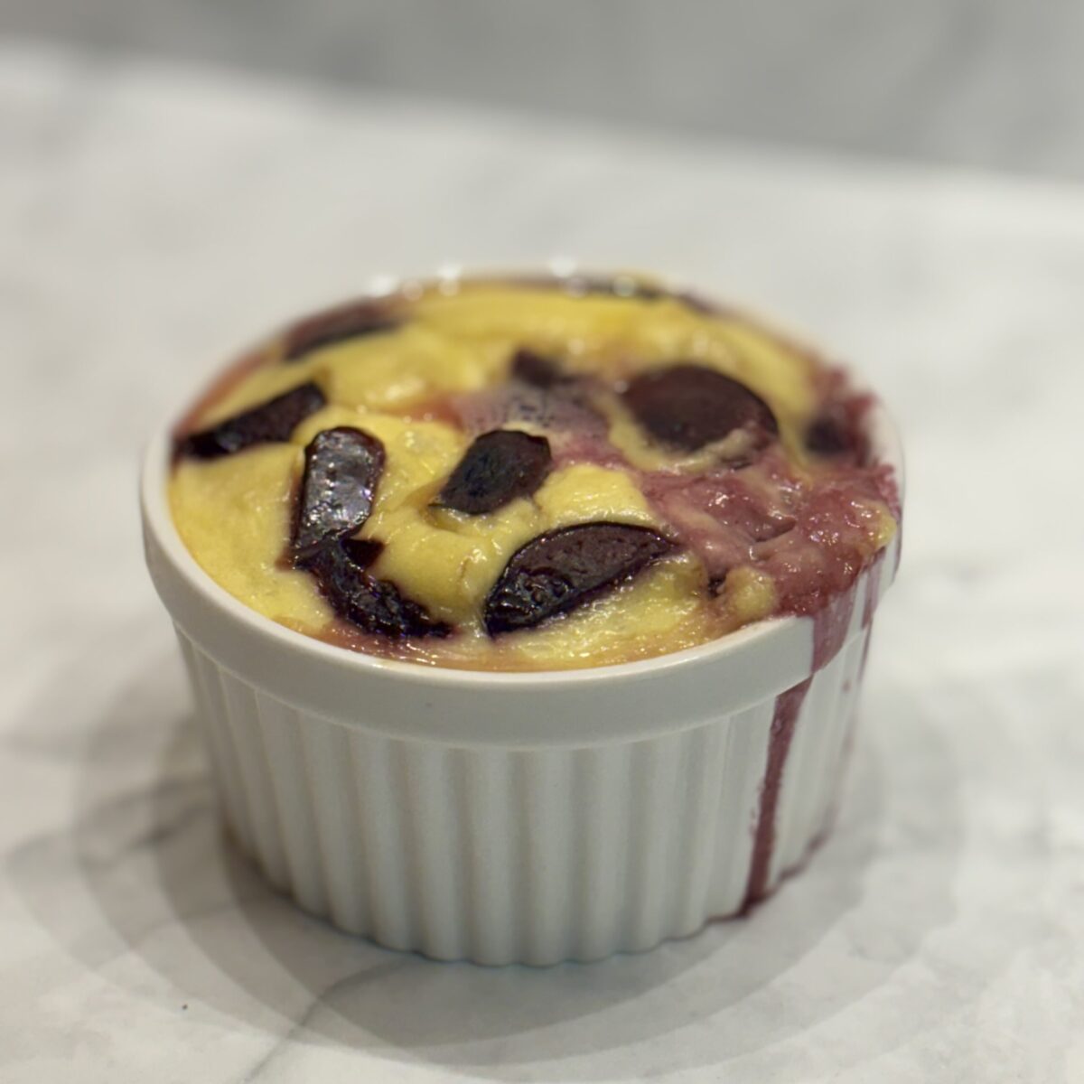 A ramekin is filled with a souffle studded with cherries.