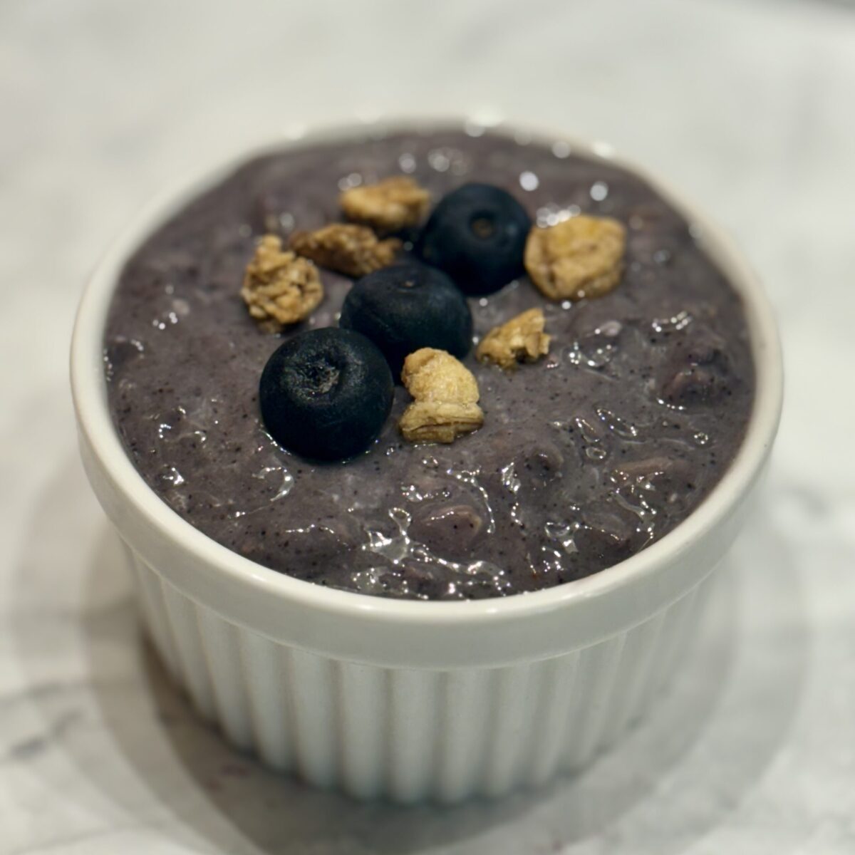 A ramekin is filled with blueberry overnight oats and topped with whole blueberries and granola.