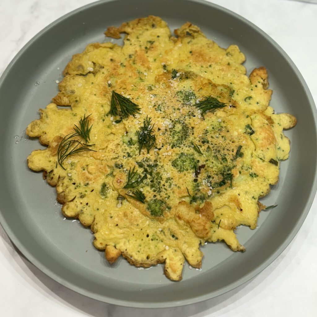 Overhead shot of a savory crepe studded with broccoli and cheese and topped with herbs.