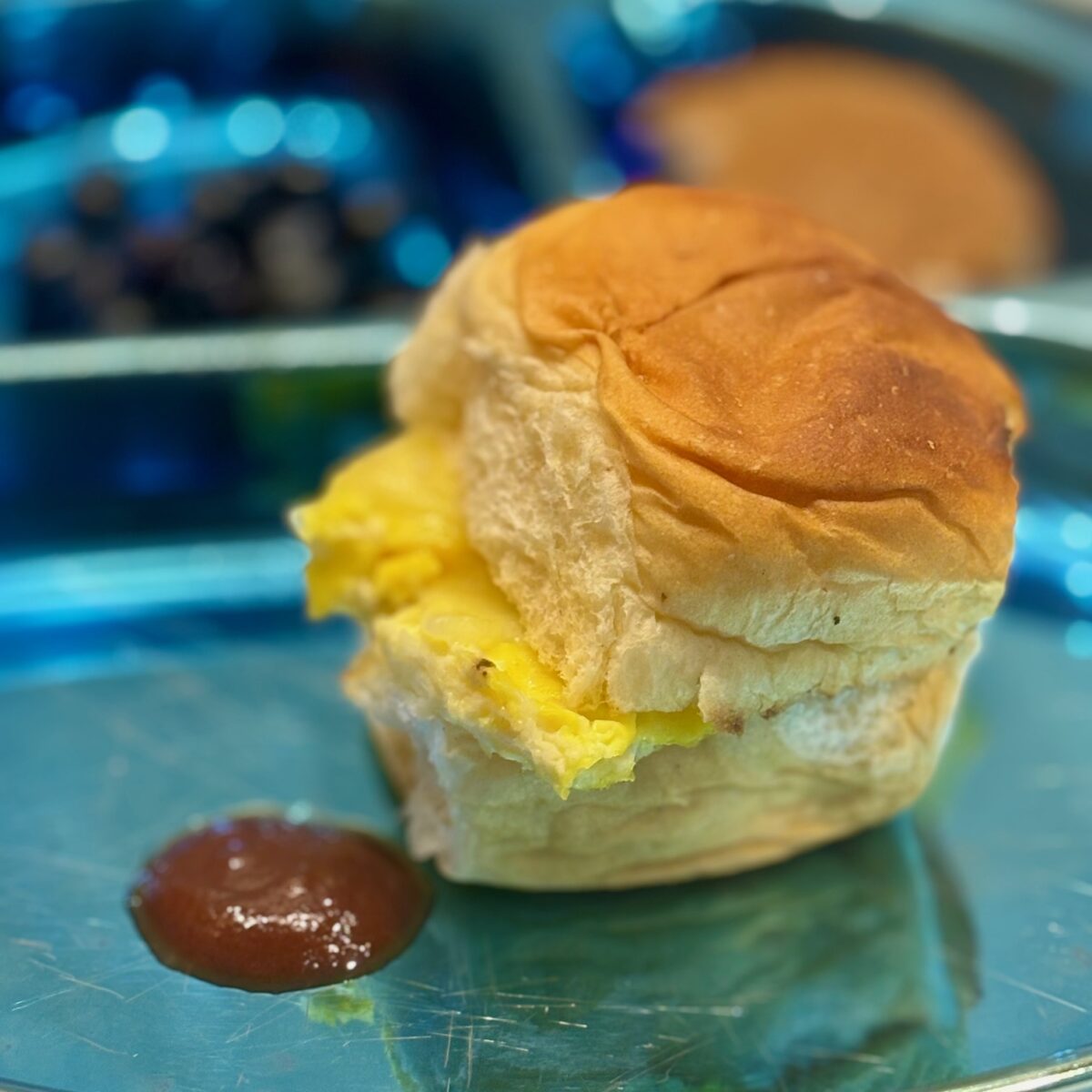 An egg and cheese sandwich, sided by a pool of ketchup, foregrounds the picture.