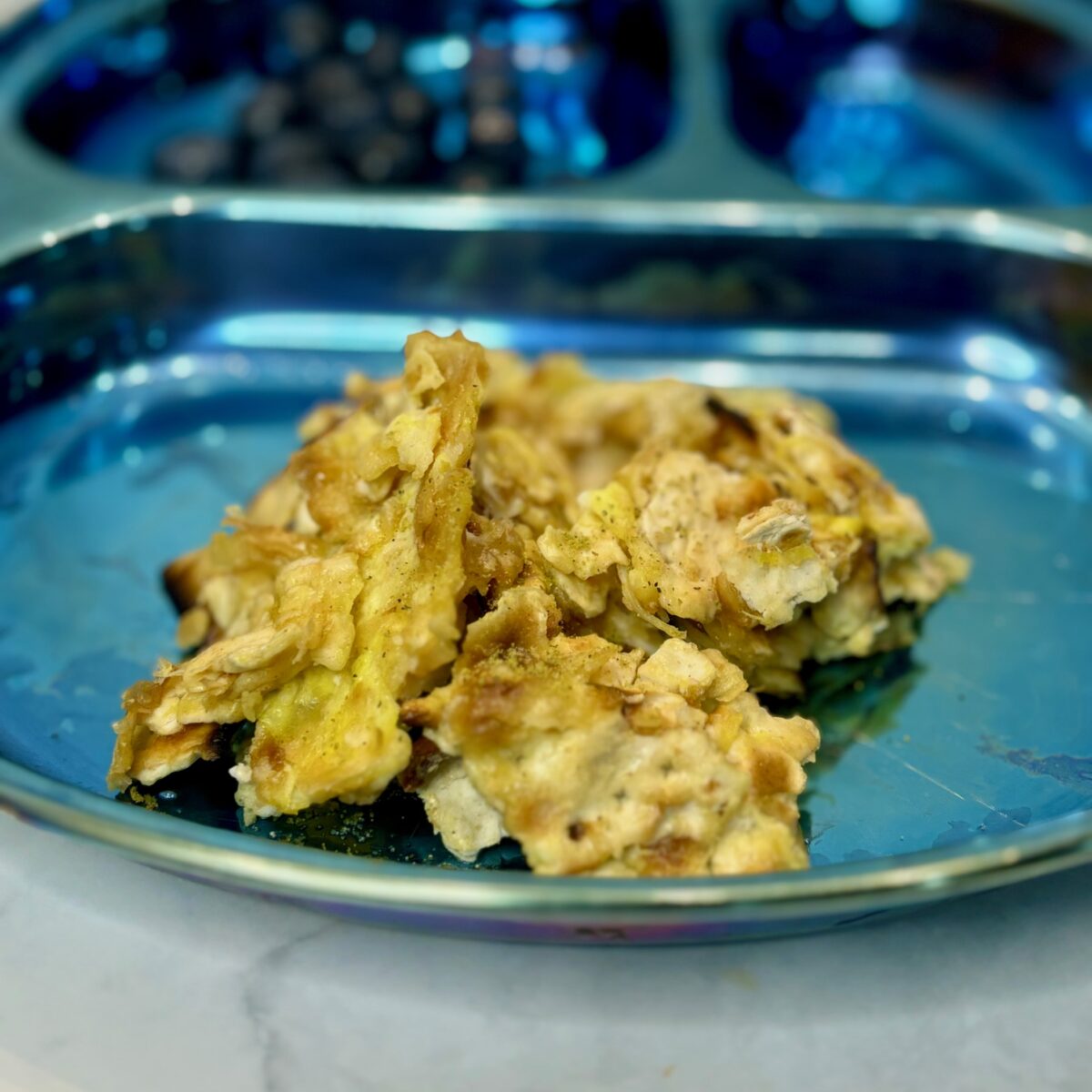 A clump of matzo brei, shards of matzoh cooked in eggs, is presented on a plate.