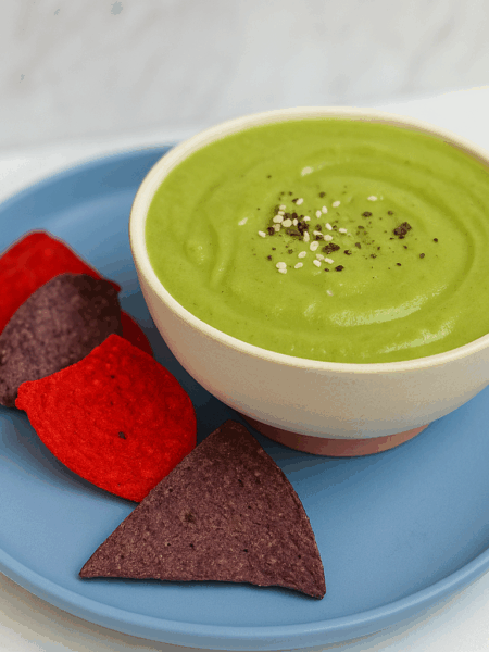 A bowl of pea soup is sided with red and blue tortilla chips.