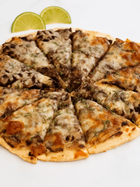 A whole pizza for toddlers is displayed, with a black bean sauce and shredded zucchini beneath the layer of cheese,
