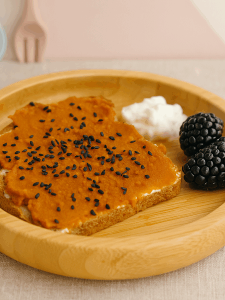 A spread of pumpkin puree, maple, orange, and ginger is shown atop cream cheese on toast.