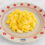 Fluffy and smooth toddler scrambled eggs are splayed out in the center of a cute plate.