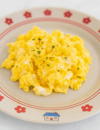 Fluffy and smooth toddler scrambled eggs are splayed out in the center of a cute plate.