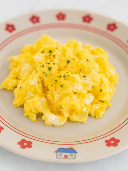 Fluffy and smooth toddler scrambled eggs are splayed out in the center of a cute plate.
