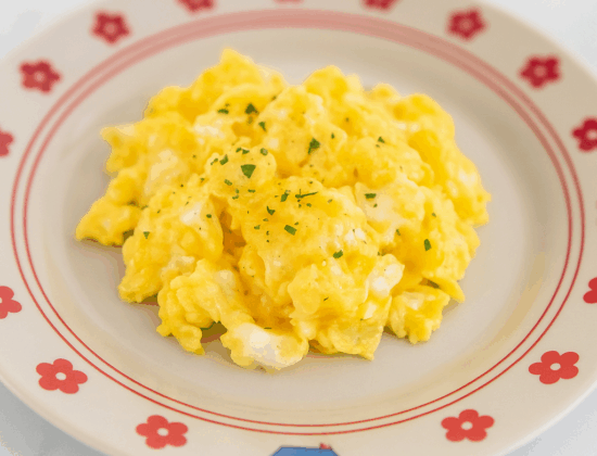 Fluffy and smooth toddler scrambled eggs are splayed out in the center of a cute plate.