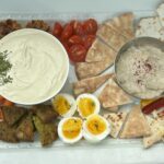 A full spread of dips, including baba ghanoush and tofu whip, alongside crackers, hardboiled eggs, and vegetables.