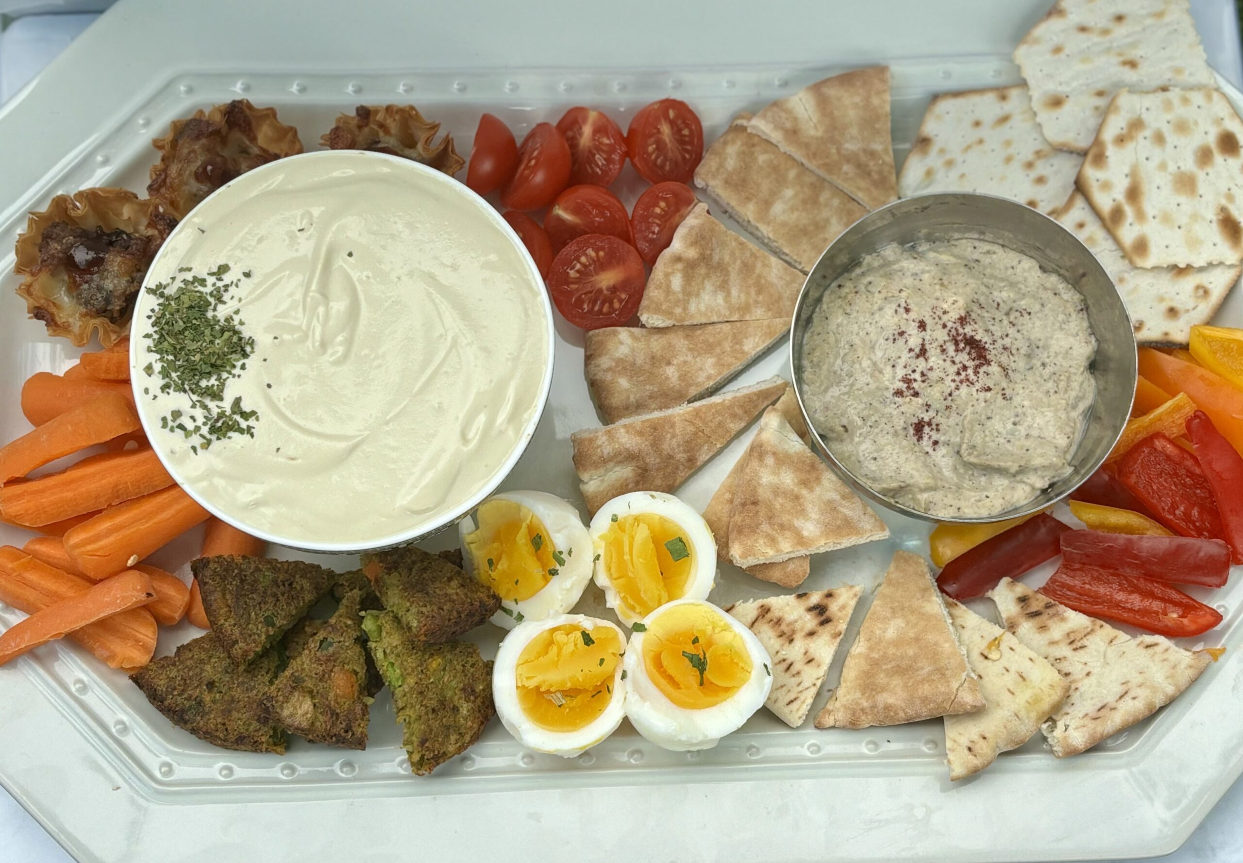 A full spread of dips, including baba ghanoush and tofu whip, alongside crackers, hardboiled eggs, and vegetables.