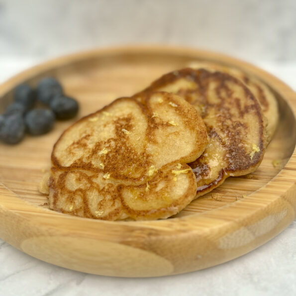 A stack of ricotta pancakes are splayed on a plate; lemon zest is sprinkled on top.