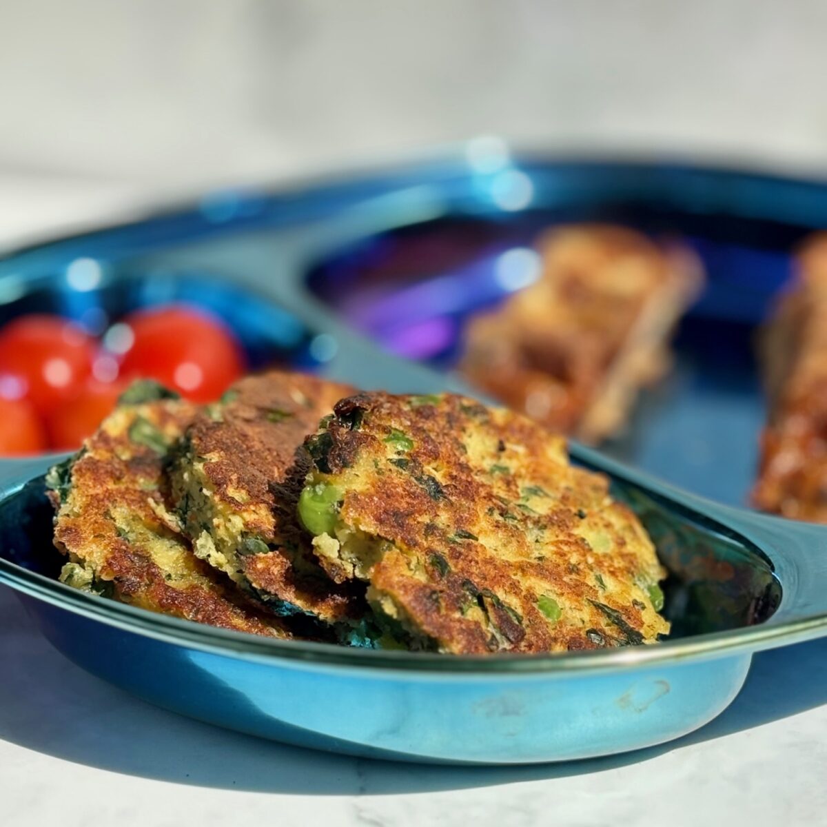 Three vegetable fritters are lined up in a side compartment of a child's plate.