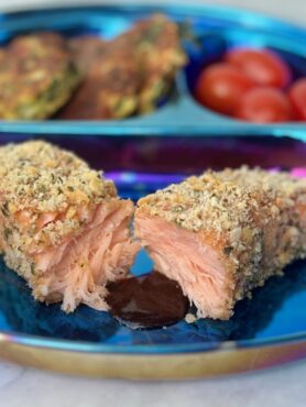 A filet of salmon crusted with crackers and cheese is split in half and fronted by a pool of barbecue sauce.