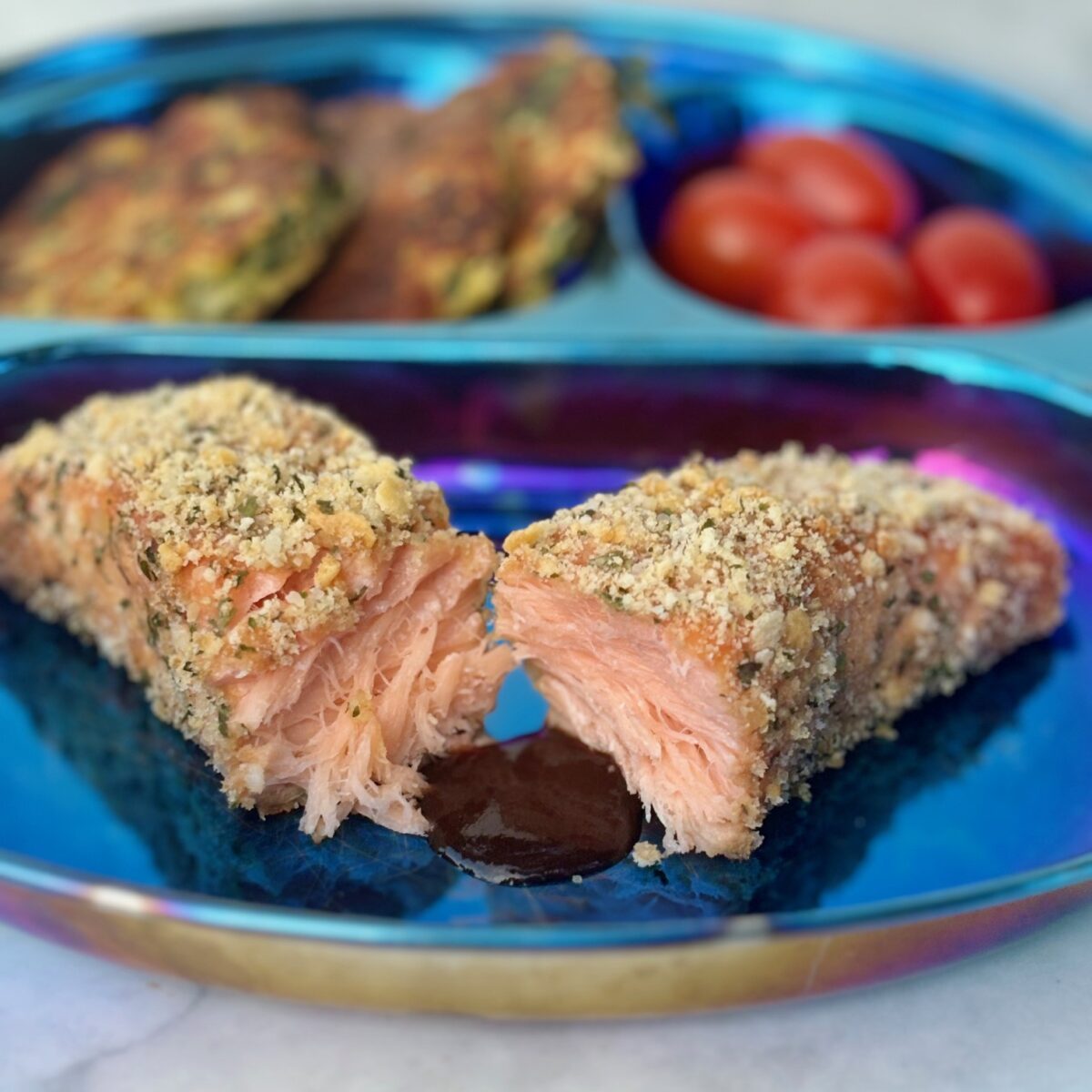 A filet of salmon crusted with crackers and cheese is split in half and fronted by a pool of barbecue sauce.