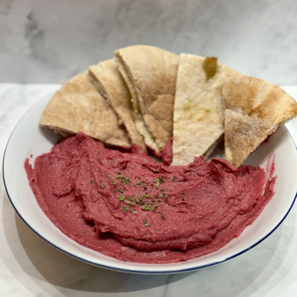 A bowl is filled with beet hummus and studded with pita triangles.