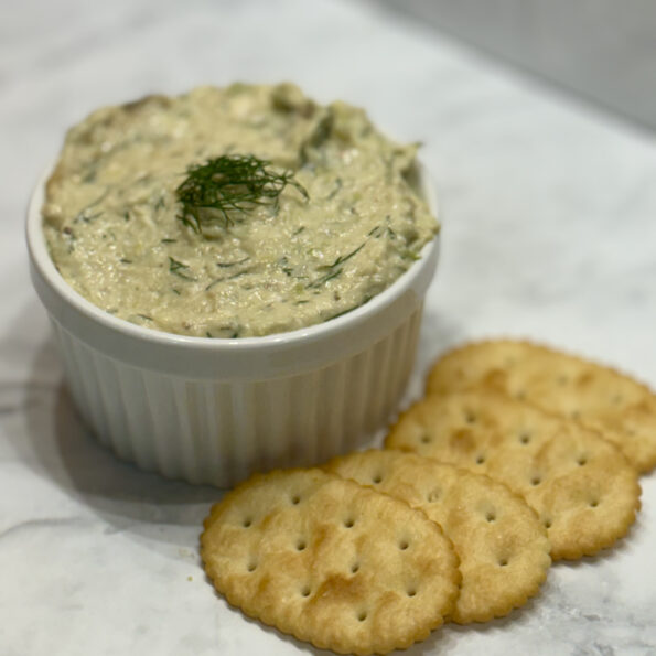 A ramekin filled with zucchini and feta spread is sided with butter crackers.