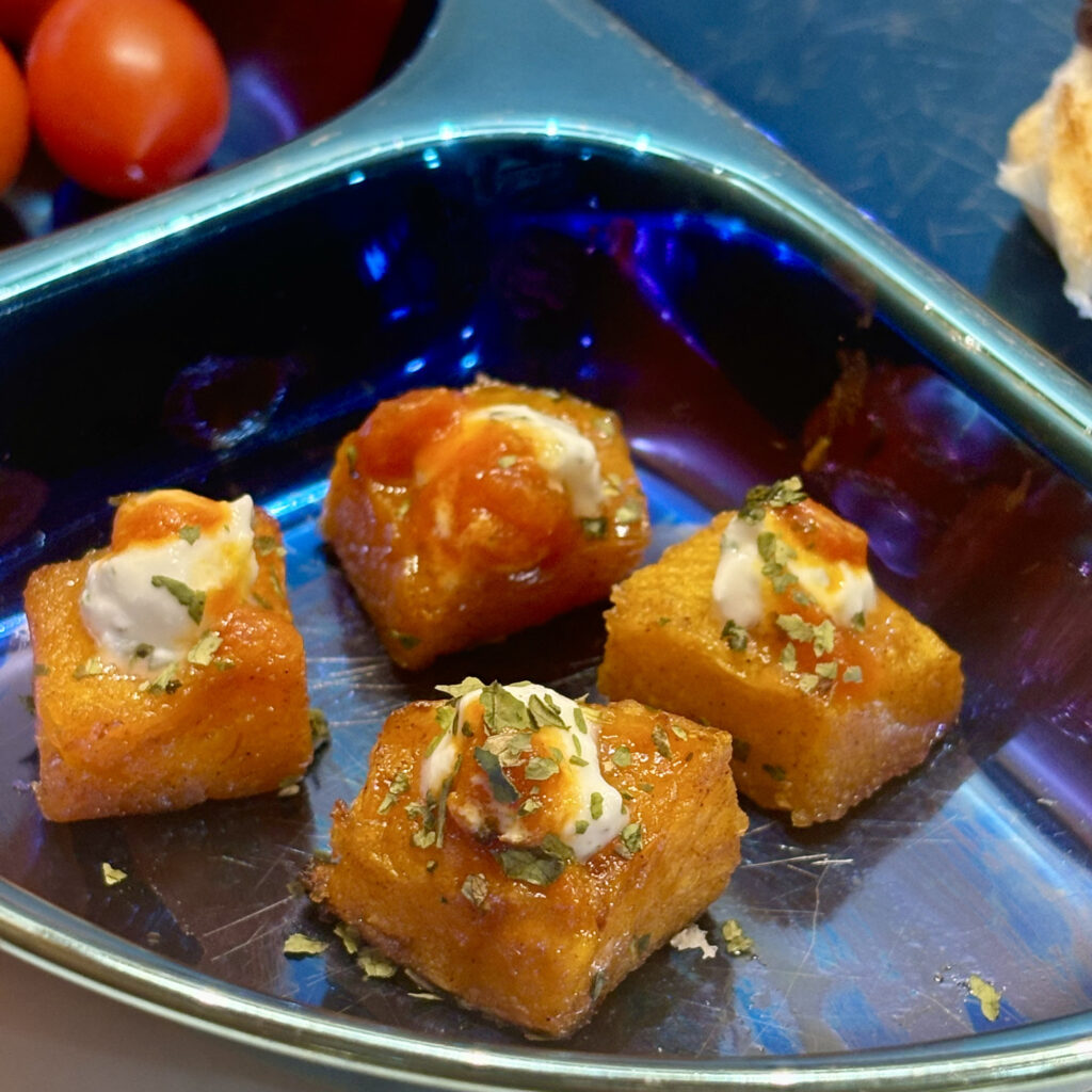 A close up of four pieces of roasted squash, topped by garlic yogurt and turmeric-stained tomato sauce.