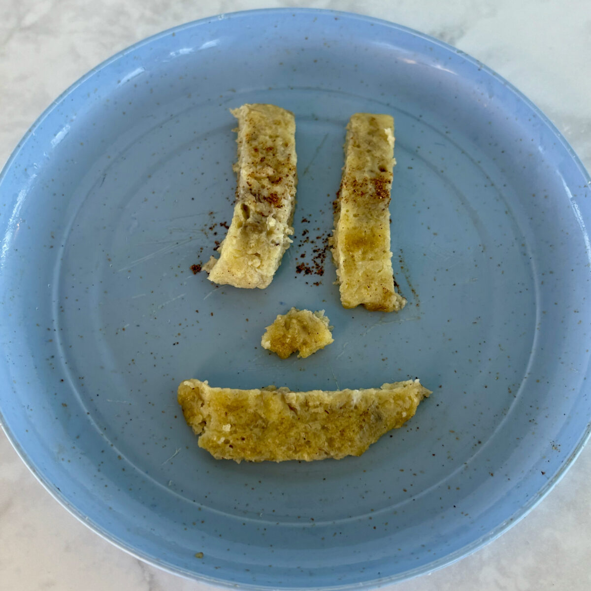 Pieces of banana pancake are arranged in a smile face on a small blue plate.