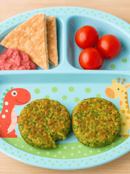 Two patties of falafel for toddlers are shown on a plate, sided by pita and tomatoes.