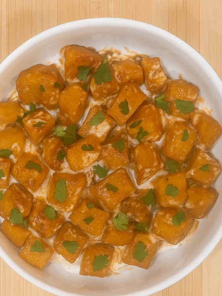 A bowl full of toddler roasted squash, topped with a mint yogurt sauce and a seasoned tomato puree.